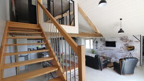 Een moderne loft met zichtbare houten balken, een trap, een keukenhoek en een zithoek met een leren bank en een fauteuil.