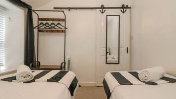 A hotel room with two beds, a mirror, a coat rack, and a sliding door.
