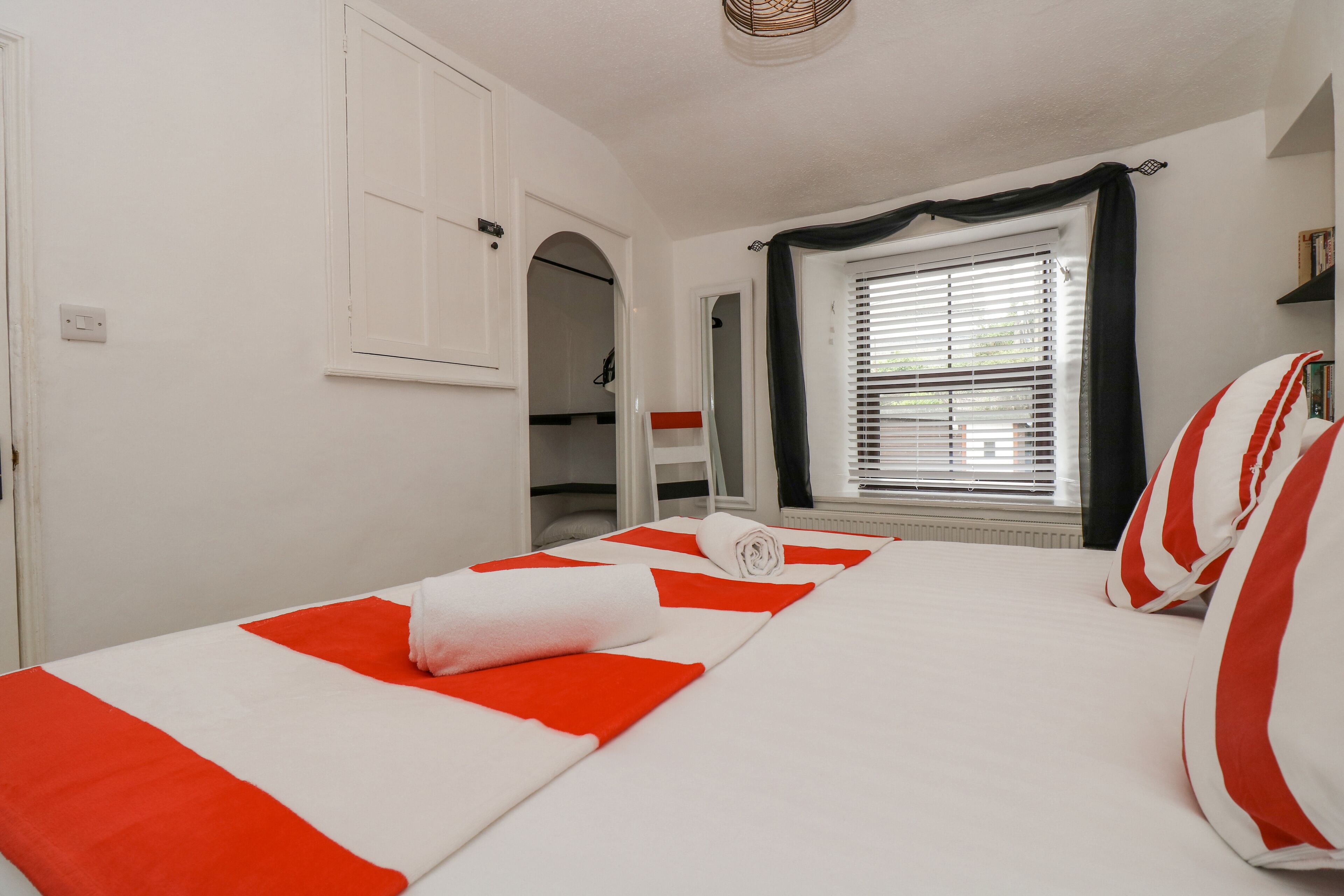 A hotel room with a bed, a window with blinds, a wardrobe, and a door.