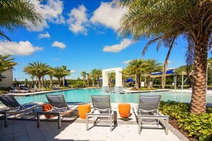 A poolside area with lounge chairs and umbrellas, surrounded by palm trees and a clear blue sky. - Relax in Style: Elegant Vacation Home in Orlando (Kissimmee)