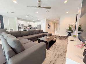 A modern living room with a sectional sofa, a coffee table, and a dining area with a kitchen in the background.