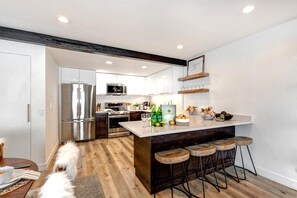 A modern kitchen with a central island, bar stools, and a dog.