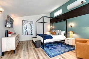 Un dormitorio moderno con una cama con dosel, un aparador de madera, una mesita pequeña, una silla y un cuadro abstracto grande en la pared.
