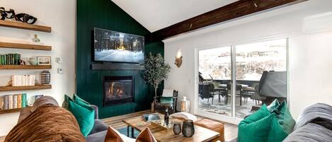 A cozy living room with a fireplace, bookshelves, and a large window offering a view of the outdoors.