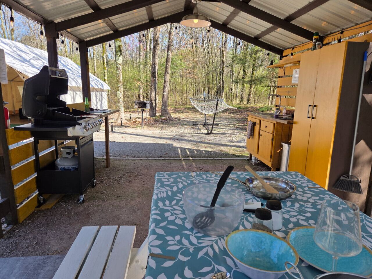 An outdoor kitchen area with a grill, a table with cooking utensils, and a hammock.