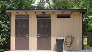 A small, single-story building with two doors, a trash bin, and a hose on the side.