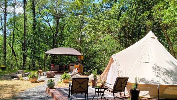 A tented camping area with a deck, chairs, and a small structure with a roof.