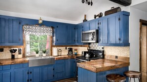 Una cocina con armarios azules, una encimera de madera, un fregadero, una estufa y dos taburetes.