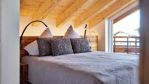A bedroom with a wooden ceiling, a large window, and a bed with patterned pillows. - Chalet Sunshine – Alpine Charm With Stunning Views (Garmisch-Partenkirchen)