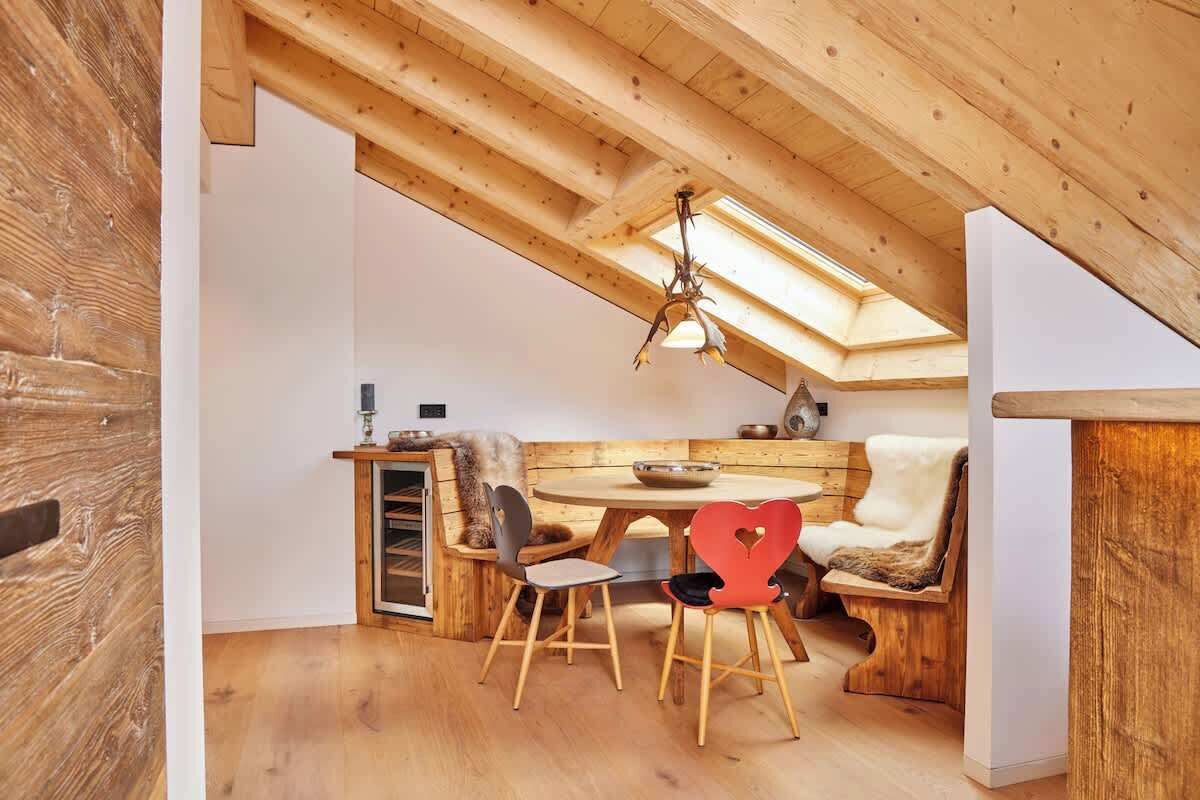 A cozy room with a wooden ceiling, a round table with chairs, and a bench with a fur throw.