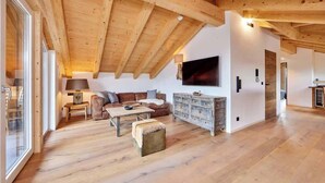 A spacious living room with wooden beams, a sofa set, a coffee table, and a television mounted on the wall. - Chalet Sunshine – Alpine Charm With Stunning Views (Garmisch-Partenkirchen)