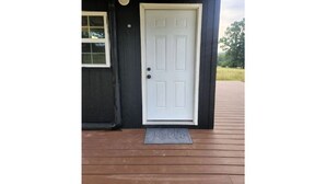 Una puerta blanca con felpudo, una ventana y una terraza de madera.