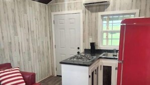 Una cocina compacta con una isla central, un refrigerador rojo y un sofá rojo con cojines a rayas.