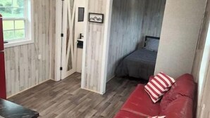 Un espacio habitable compacto con un sofá de cuero rojo, una cama pequeña y una zona de kitchenette.