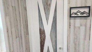 Un pasillo con una puerta blanca que presenta un diseño grande en forma de 'X', paredes de madera y un cuadro en la pared.