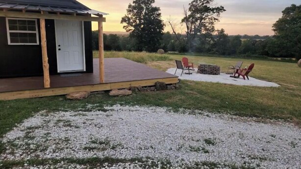 Una cabaña pequeña con una terraza de madera, un brasero y mobiliario exterior.