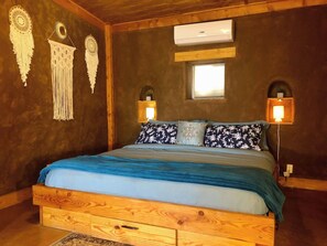 A wooden-framed bed with a blue and white bedspread, two wall-mounted lamps, and wall decorations. - Unique Strawbale/Hueco Tanks/Mtn Views/King BD (El Paso)