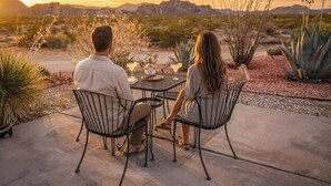 Una pareja cenando en una mesa al aire libre con vistas a un paisaje desértico y montañas al fondo.