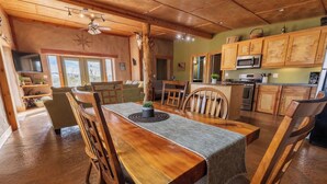 Un comedor amplio con una mesa y sillas de madera, un ventilador de techo y vista al área de la cocina.