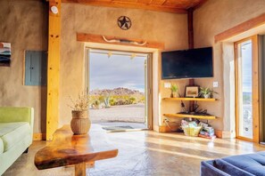 A room with a wooden ceiling, a television mounted on the wall, a wooden bench, a green sofa, and a door leading outside. - Unique Strawbale/Hueco Tanks/Mtn Views/King BD (El Paso)