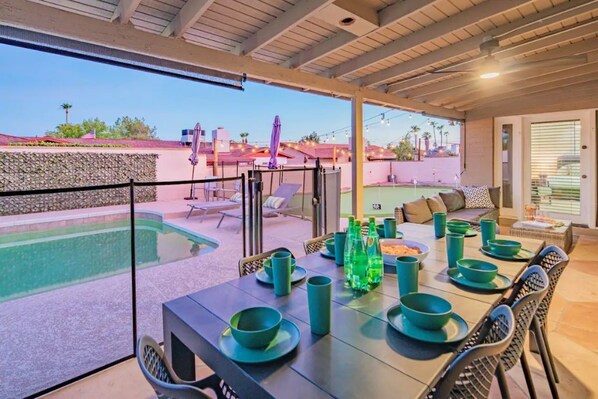 Un espace extérieur aménagé pour les repas, avec une piscine, un coin salon couvert et une vue sur le quartier.