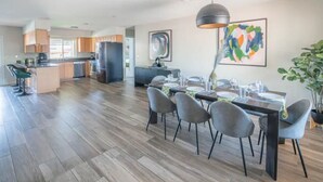 Eine moderne Küche mit Holzboden, einem Essbereich mit grauen Stühlen und einem großen, abstrakten Gemälde an der Wand.