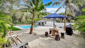 Un jardin avec une piscine, un espace barbecue et un coin salon abrité.