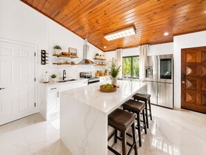 Una cocina moderna con armarios blancos, techo de madera y una isla grande con taburetes.