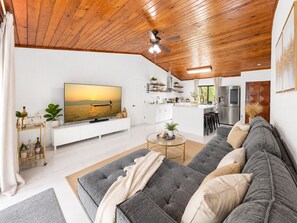 A modern living room with a large flat-screen TV, a grey sofa, and a wooden ceiling.