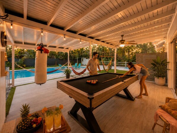 An indoor pool area with a pool table, chairs, and a hammock.