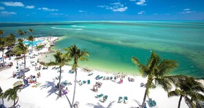 A beach resort with white sand, palm trees, and clear turquoise waters.