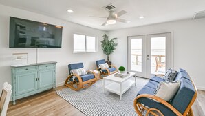 A living room with a television, wicker furniture, a coffee table, and a view to the outside. - NEW! Bayfront home w/ private pier, steps to beach (Freeport)