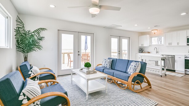 A spacious living room with a white coffee table, blue sofa, and wicker chairs. - NEW! Bayfront home w/ private pier, steps to beach (Freeport)