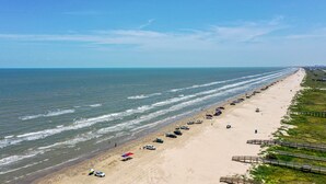 A beach with a long stretch of sand, a row of parked cars, and a wooden boardwalk. - NEW! Bayfront home w/ private pier, steps to beach (Freeport)