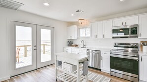 A modern kitchen with white cabinets, stainless steel appliances, and a view through a sliding door to an outdoor deck. - NEW! Bayfront home w/ private pier, steps to beach (Freeport)