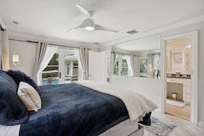 Ein Schlafzimmer mit Bett, Deckenventilator, großem Fenster mit Vorhängen und Blick auf einen Außenpool.