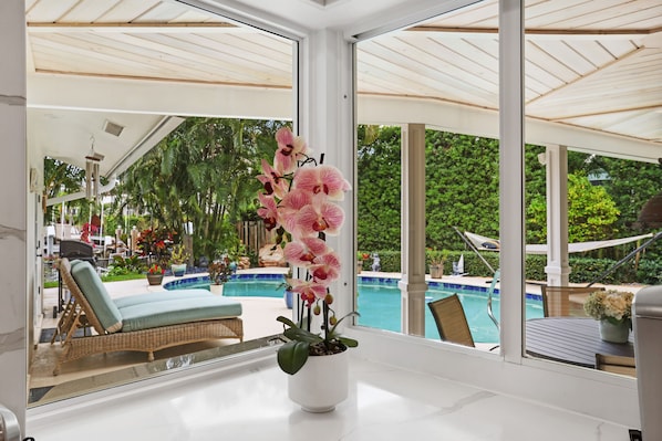 Ein modernes Zimmer mit großem Fenster und Blick auf einen Pool und üppiges Grün.