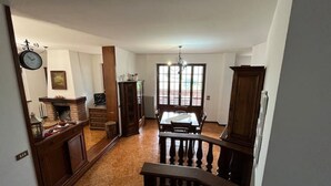 Een ruime woonkamer met een eettafel, een open haard en een trap naar een hoger gelegen verdieping.