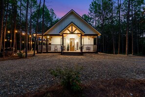 A cabin with a welcoming entrance, surrounded by a gravel driveway and a forested area. - A Perfect Landing - Luxury & Incredible Location (Broken Bow)