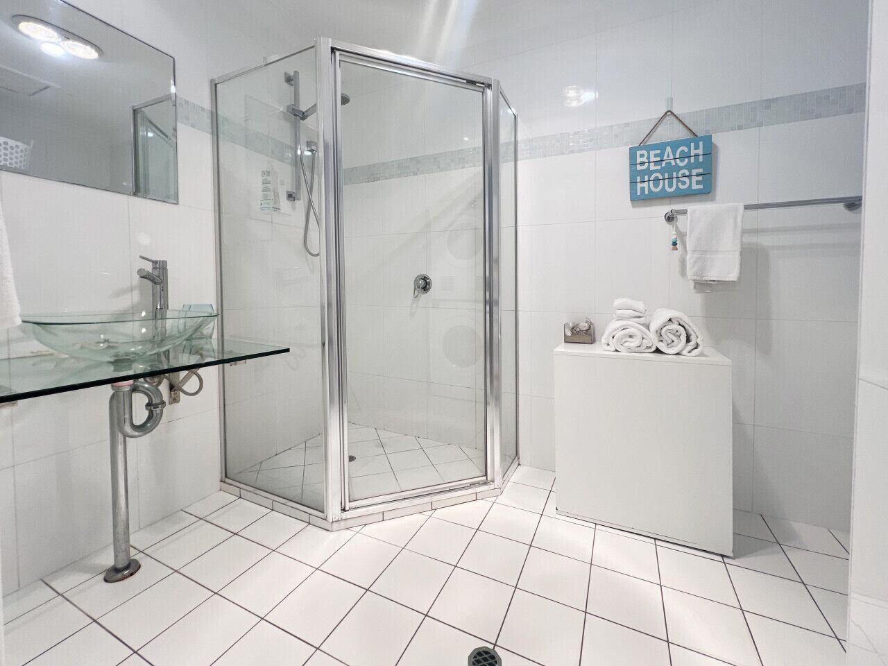 Un bagno moderno con cabina doccia in vetro, lavabo in vetro e porta asciugamani con asciugamani piegati.