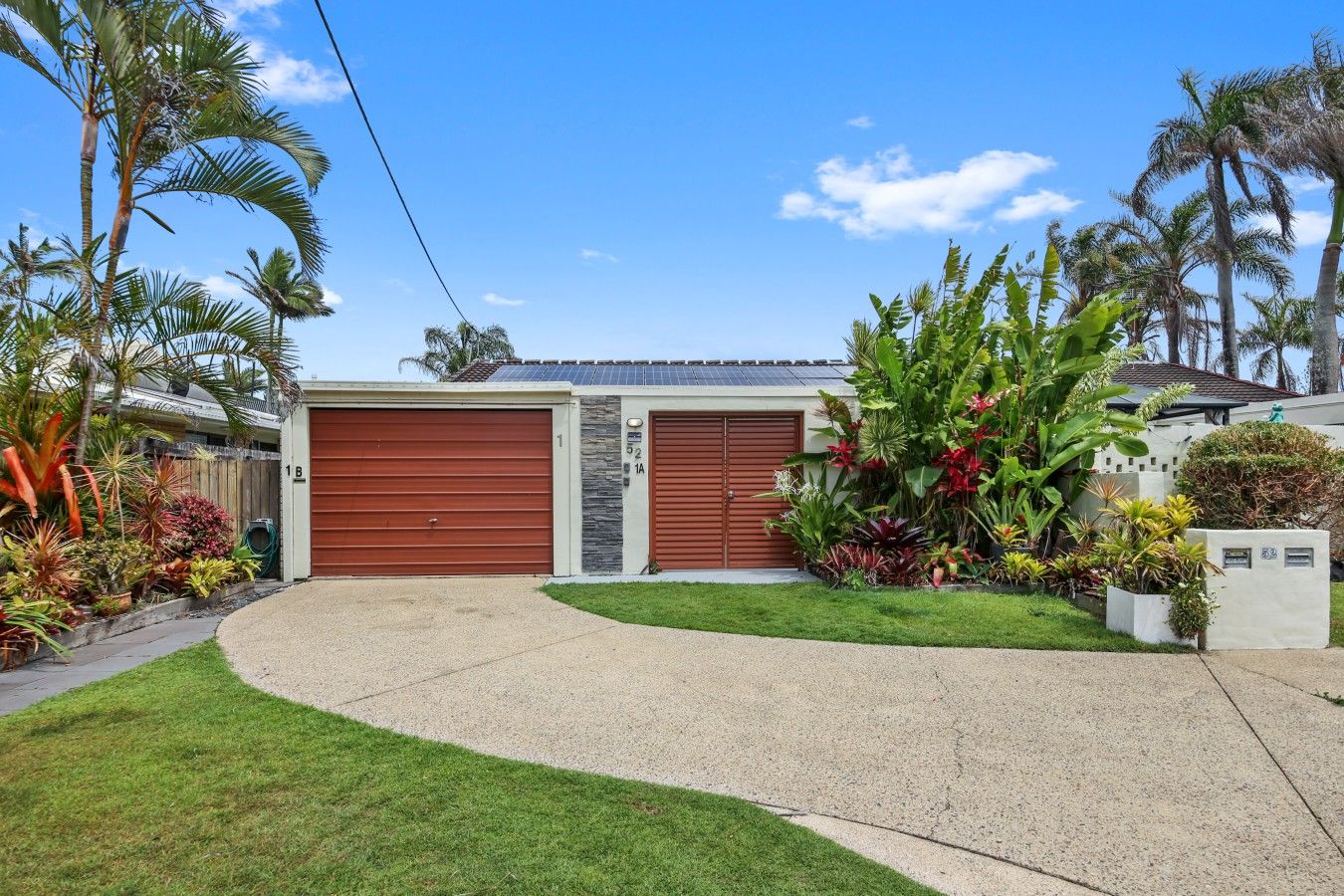 A residential house with two garage doors, a well-maintained lawn, and tropical plants.