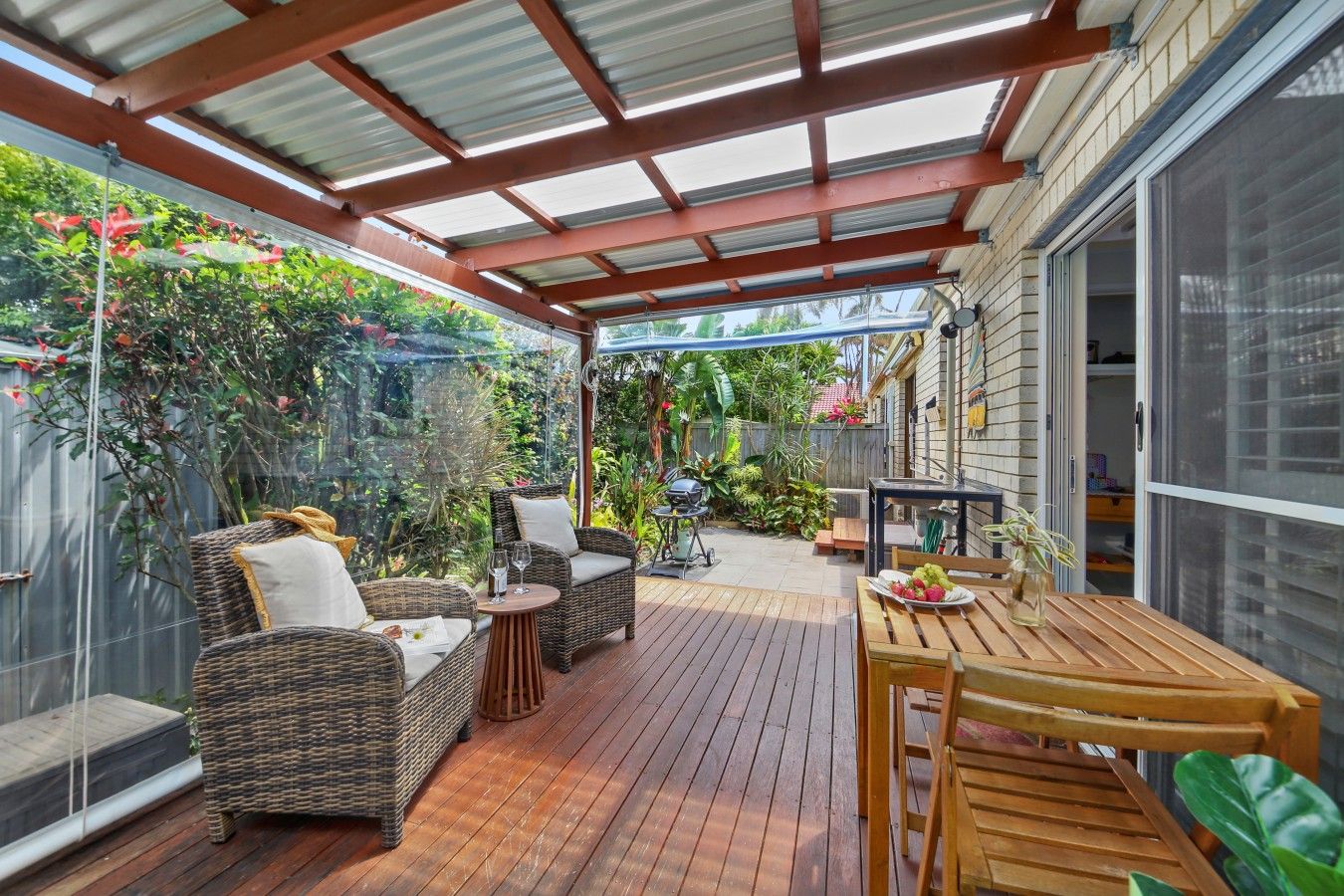 A covered patio with wicker furniture, a wooden table, and a grill.