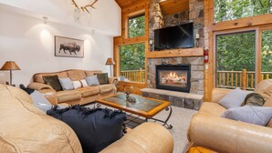 A cozy living room with a stone fireplace, leather sofas, and a large TV.