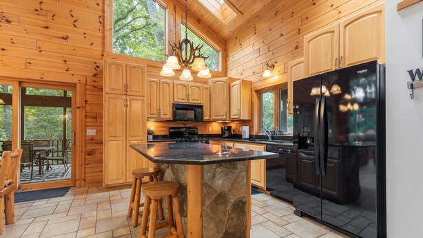 A spacious kitchen with wooden cabinets, a large island with stools, a black refrigerator, and a stone countertop.