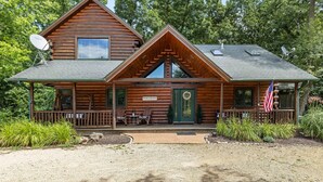 A log cabin with a porch, a welcome sign, and an American flag.