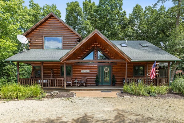 A log cabin with a porch, two rocking chairs, and an American flag. - Secluded Spacious Cabin with Large Bedrooms and Huge Deck & Hot Tub (Galena)