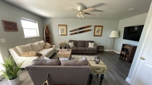 A living room with a beige sofa, a brown sofa, a coffee table, a ceiling fan, and a television on the wall. - Sunrise Bluff Lakefront - in family-friendly area w/ great view of Grand Lake (Grove)