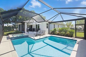 A covered outdoor swimming pool with two separate sections, a patio area with lounge chairs, and a view of a house in the background. - Chic canal-front home with dock, enclosed lanai, WiFi, A/C, bikes, & W/D (Marco Island)