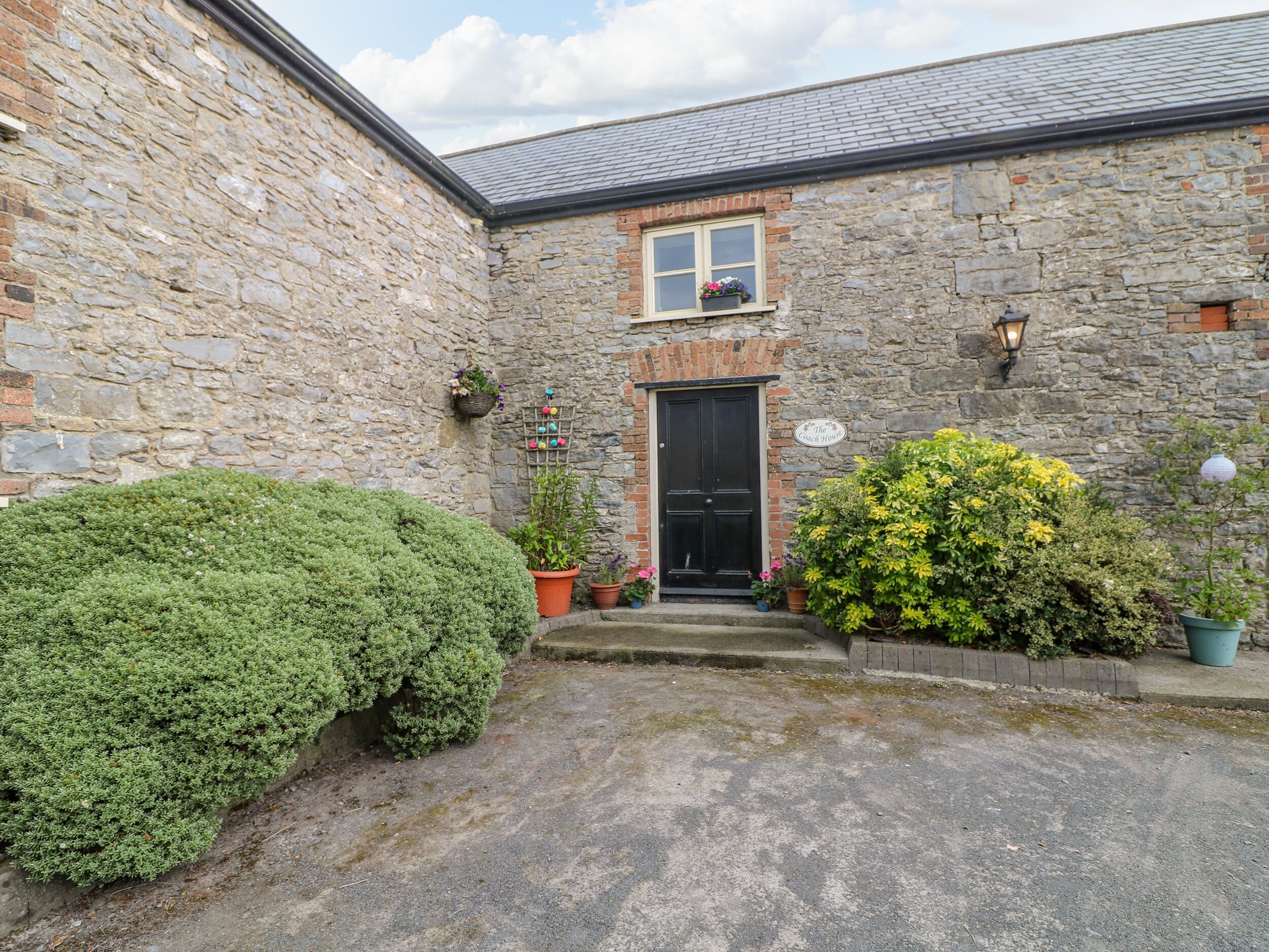 A stone building with a black door, potted plants, and a sign reading "The Coach House".