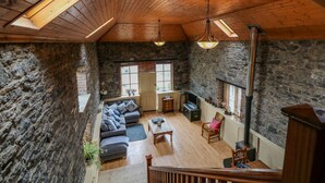 A spacious loft with exposed wooden beams, stone walls, a cozy seating area with a sofa and armchairs, and a fireplace.